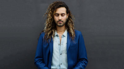Man standing against black backdrop with eyes closed wearing blue blazer and light blue button up